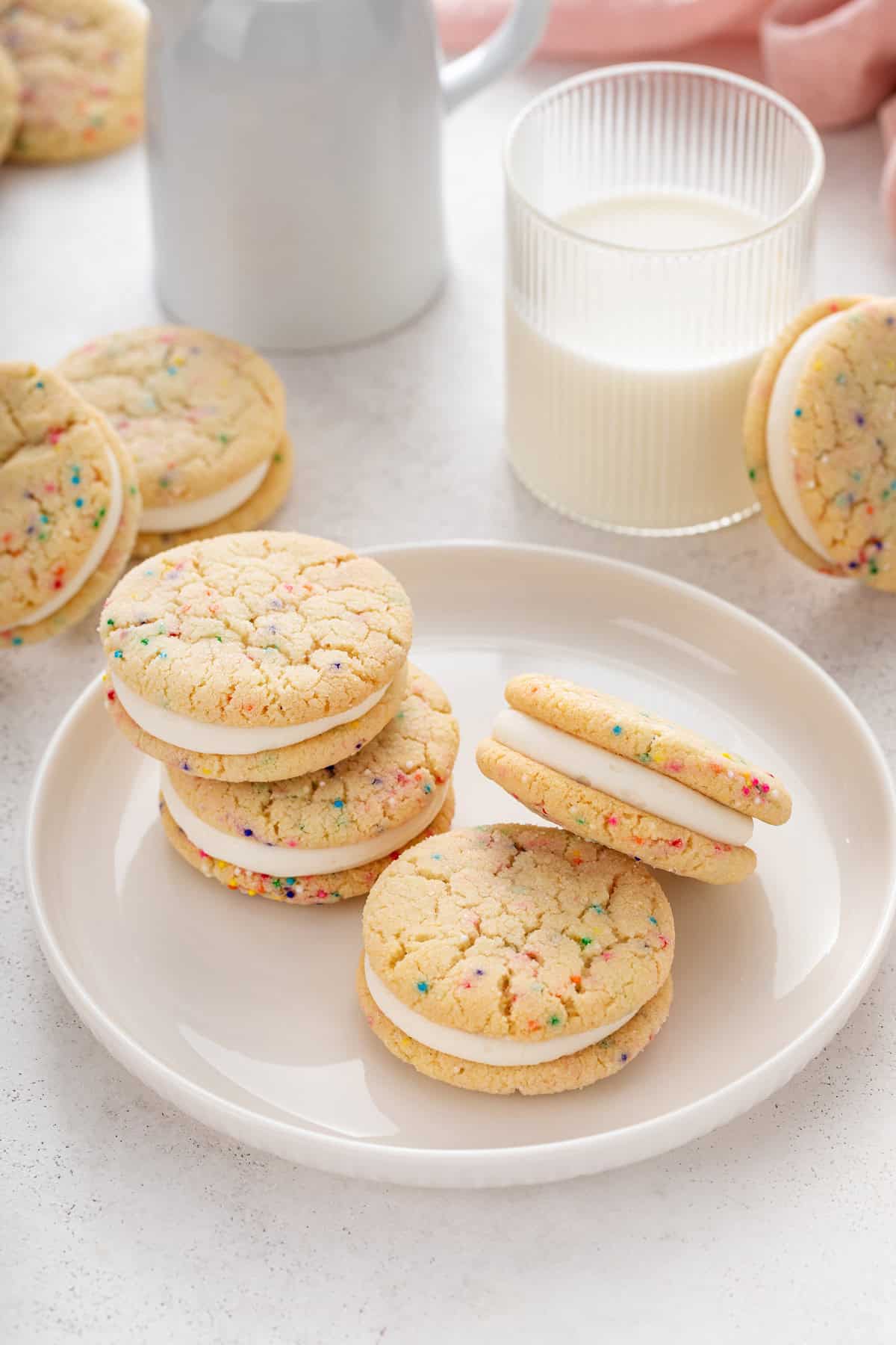 Four easy sugar cookie sandwiches arranged on a white plate next to a glass of milk.