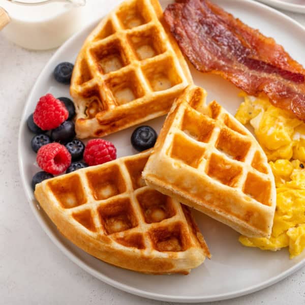 Homemade waffles on a plate with eggs and bacon.