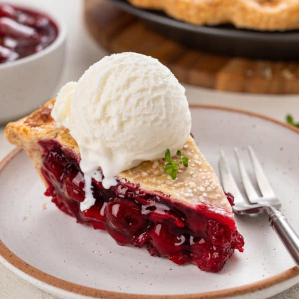Slice of sour cherry pie with a scoop of vanilla ice cream on top.