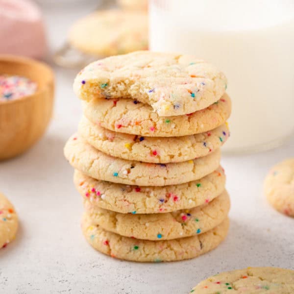 Several easy sugar cookies stacked in front of a glass of milk.