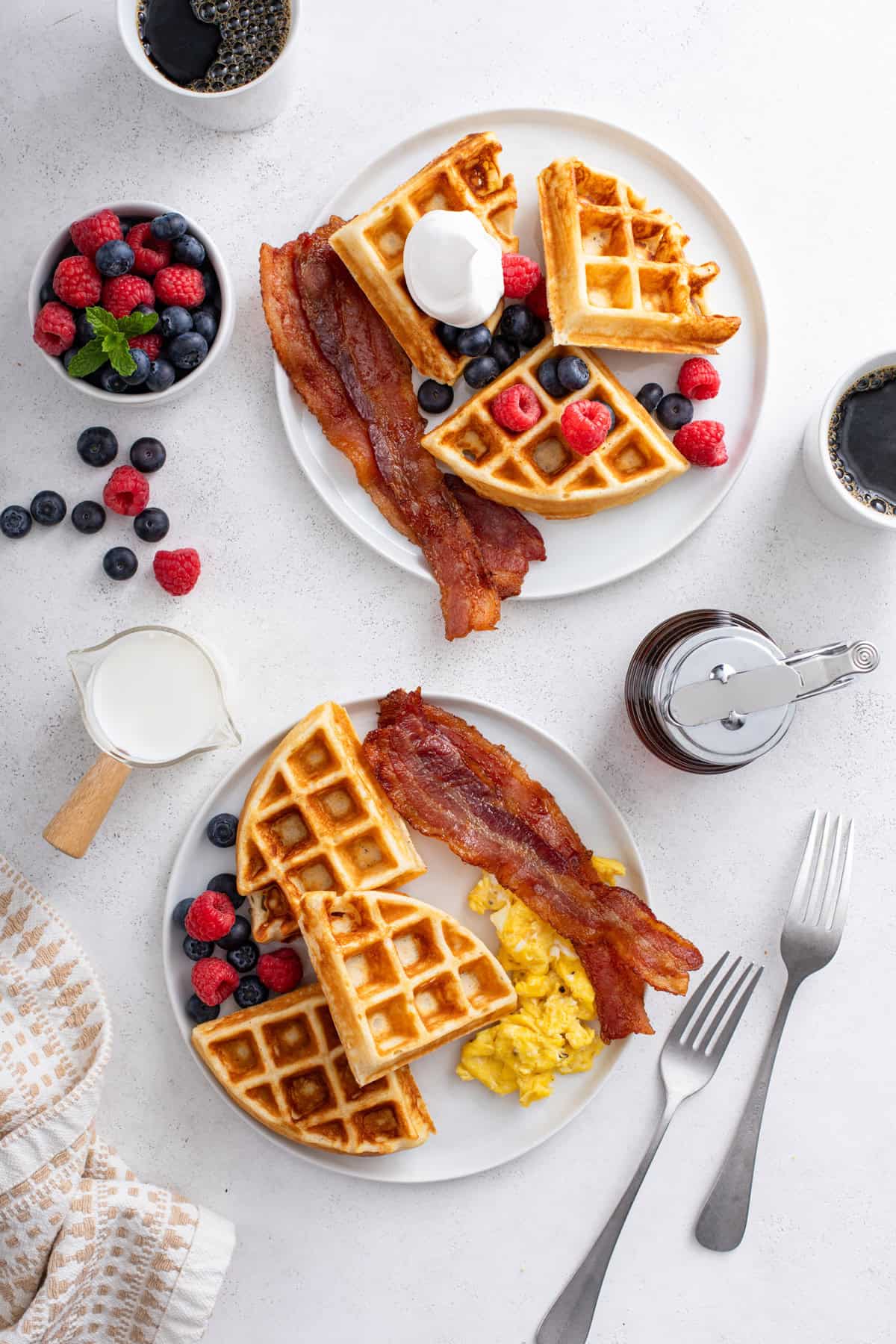 Overhead view of two white plates, each holding homemade waffles, bacon, and fresh berries.