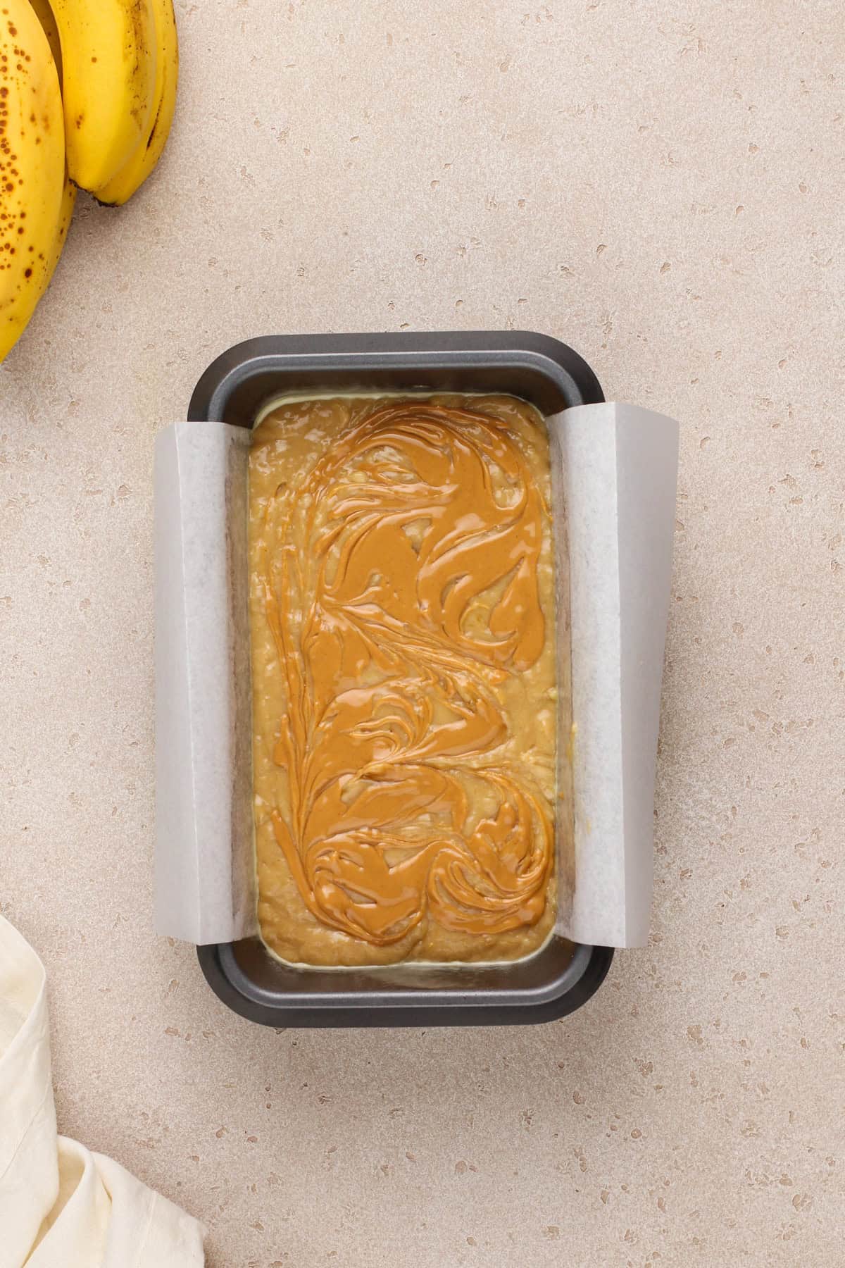Peanut butter swirled into the top of peanut butter banana bread batter in a loaf pan.