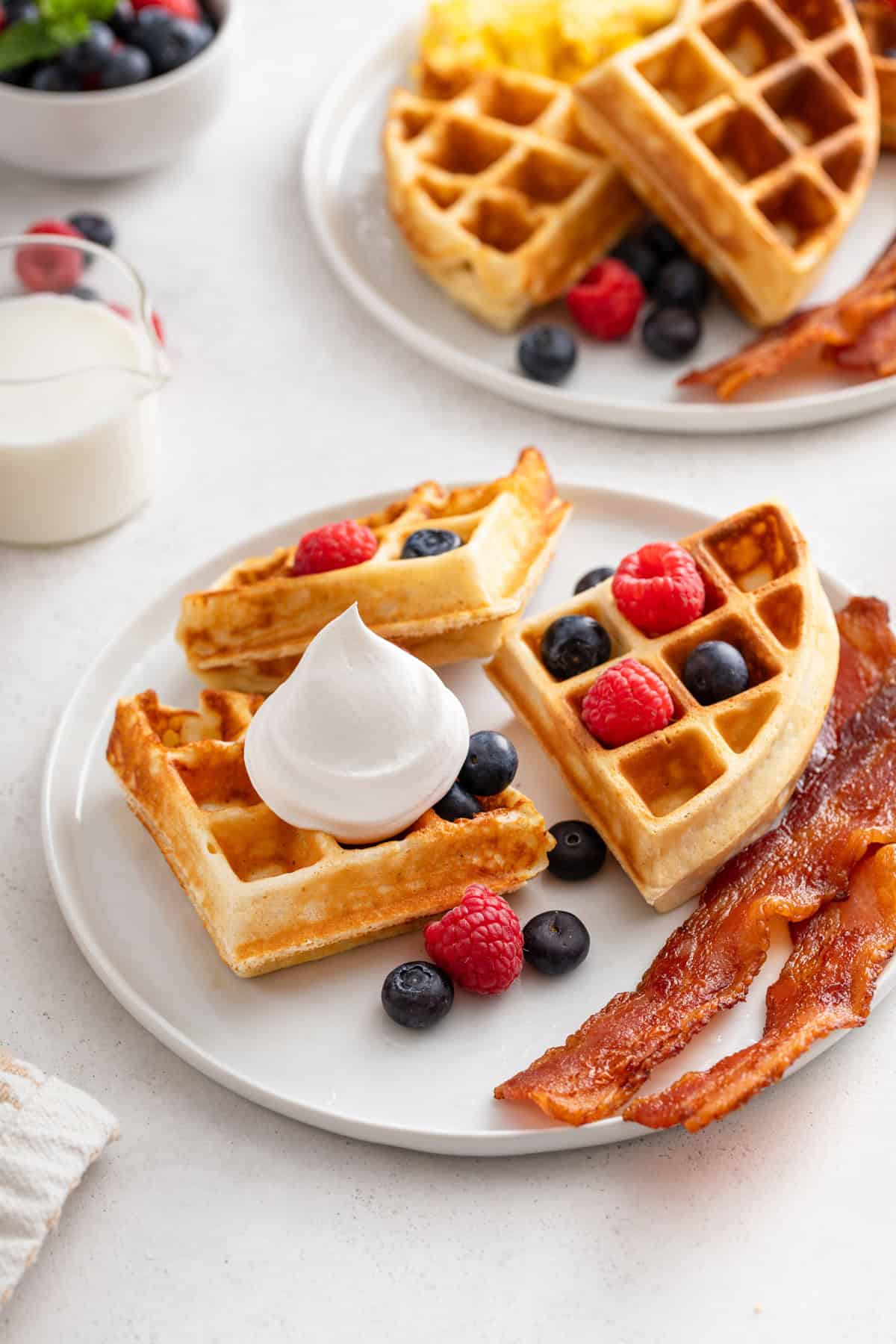 Dollop of whipped cream and fresh berries on a homemade waffle set next to bacon on a plate.