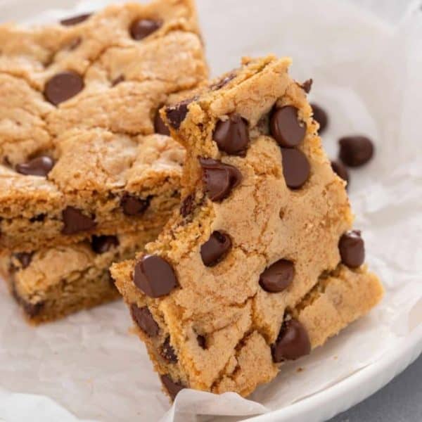 Chocolate chip cookie bar with a bite taken from it leaning against a stack of cookie bars on a white plate.