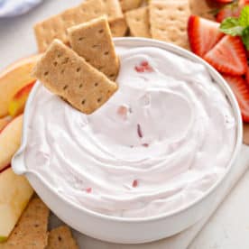 Bowl of yogurt fruit dip with two graham crackers in it.