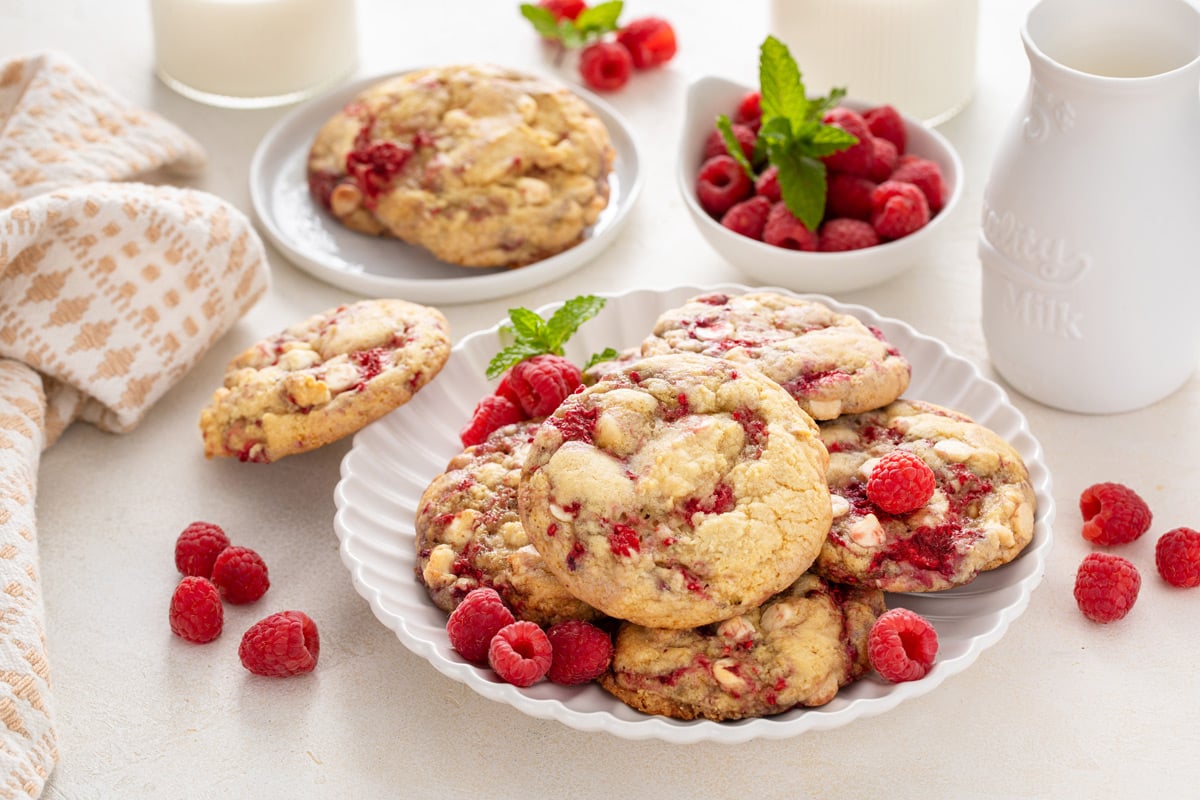 Plated white chocolate raspberry cookies with a bowl of fresh raspberries in the background.