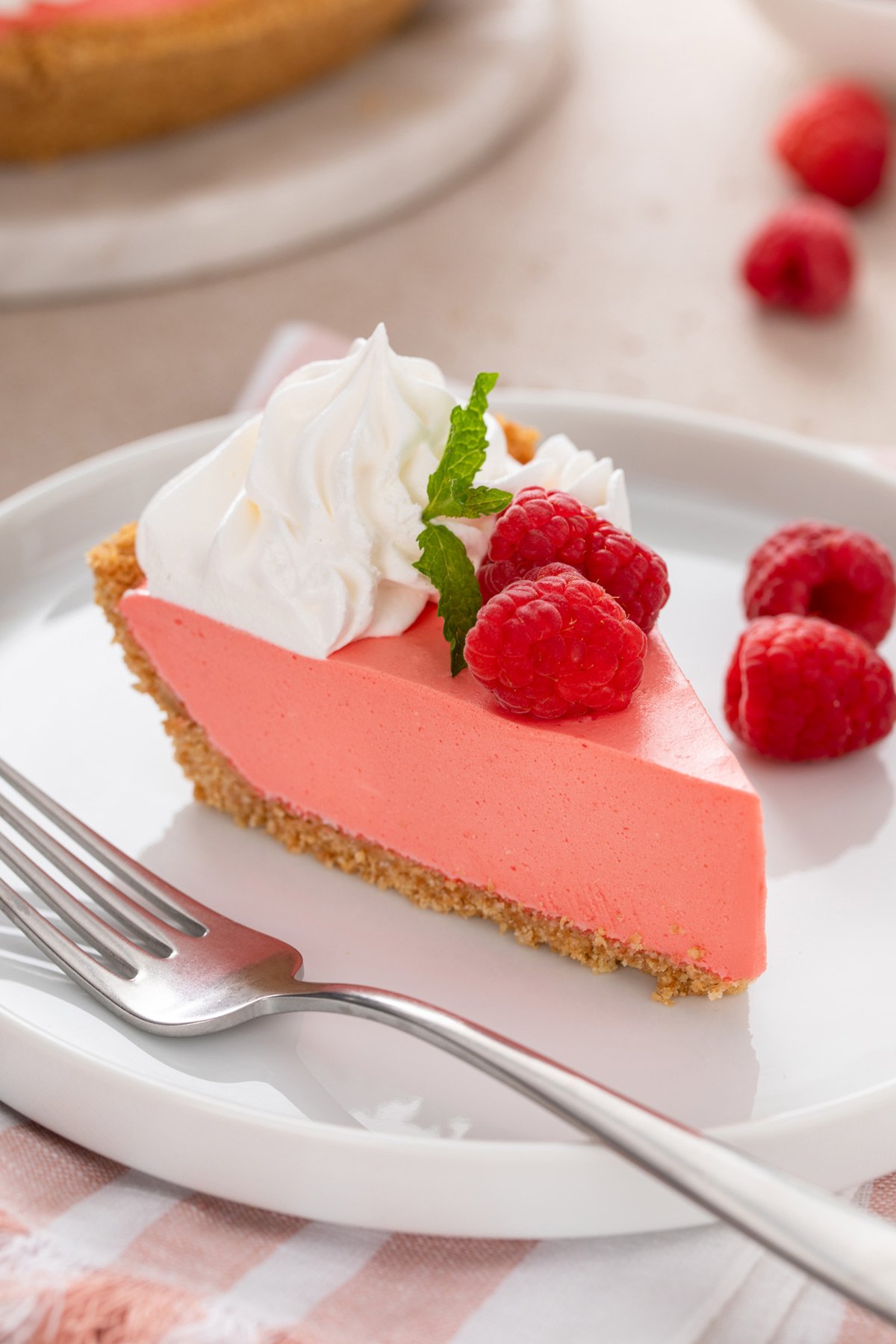 Close up of a slice of jello pie next to a fork on a white plate.