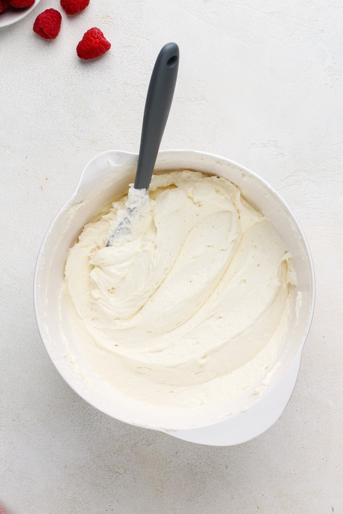 Whipped topping folded into cream cheese mixture in a white bowl.