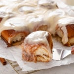 Cake server about to lift a hawaiian roll cinnamon roll.