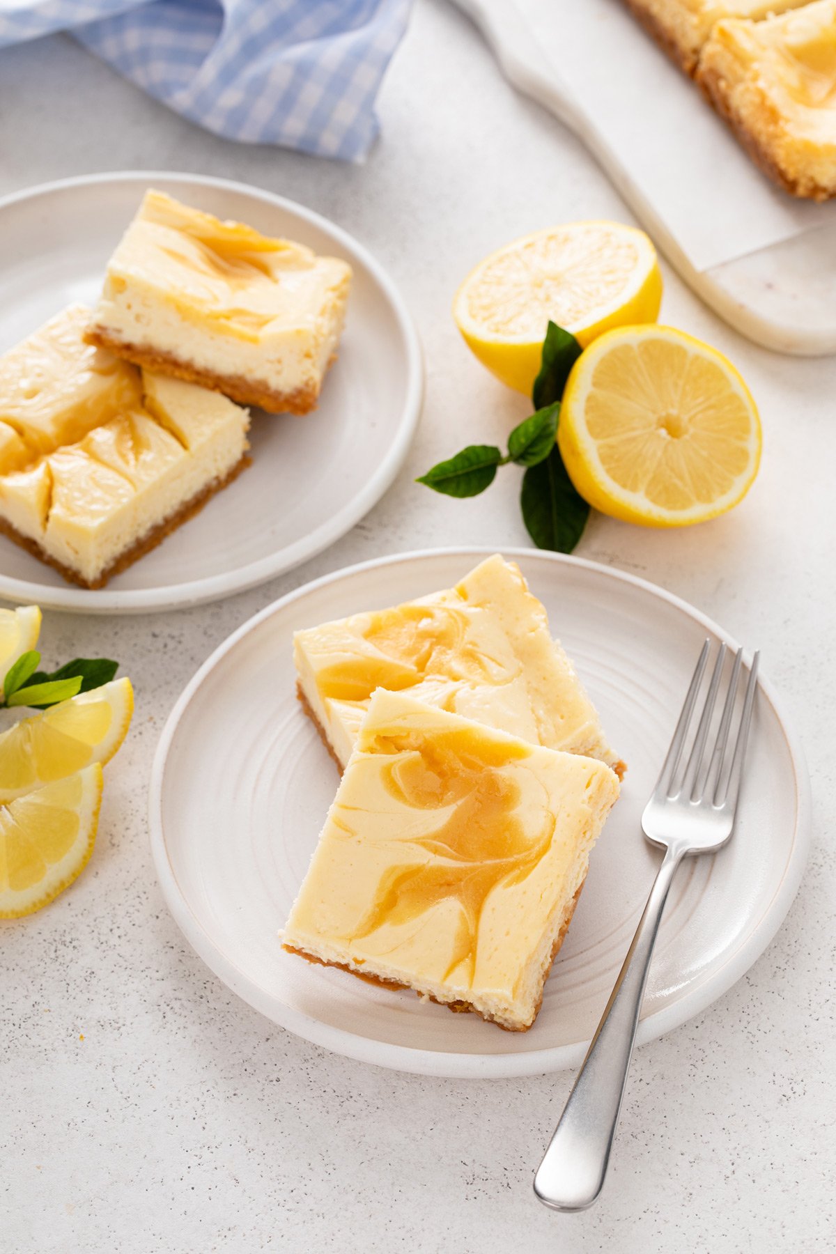 Two white plates, each holding two lemon cheesecake bars.
