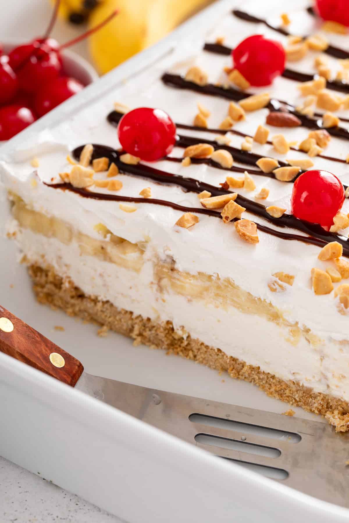 Side view of sliced banana split cake in a white baking dish.
