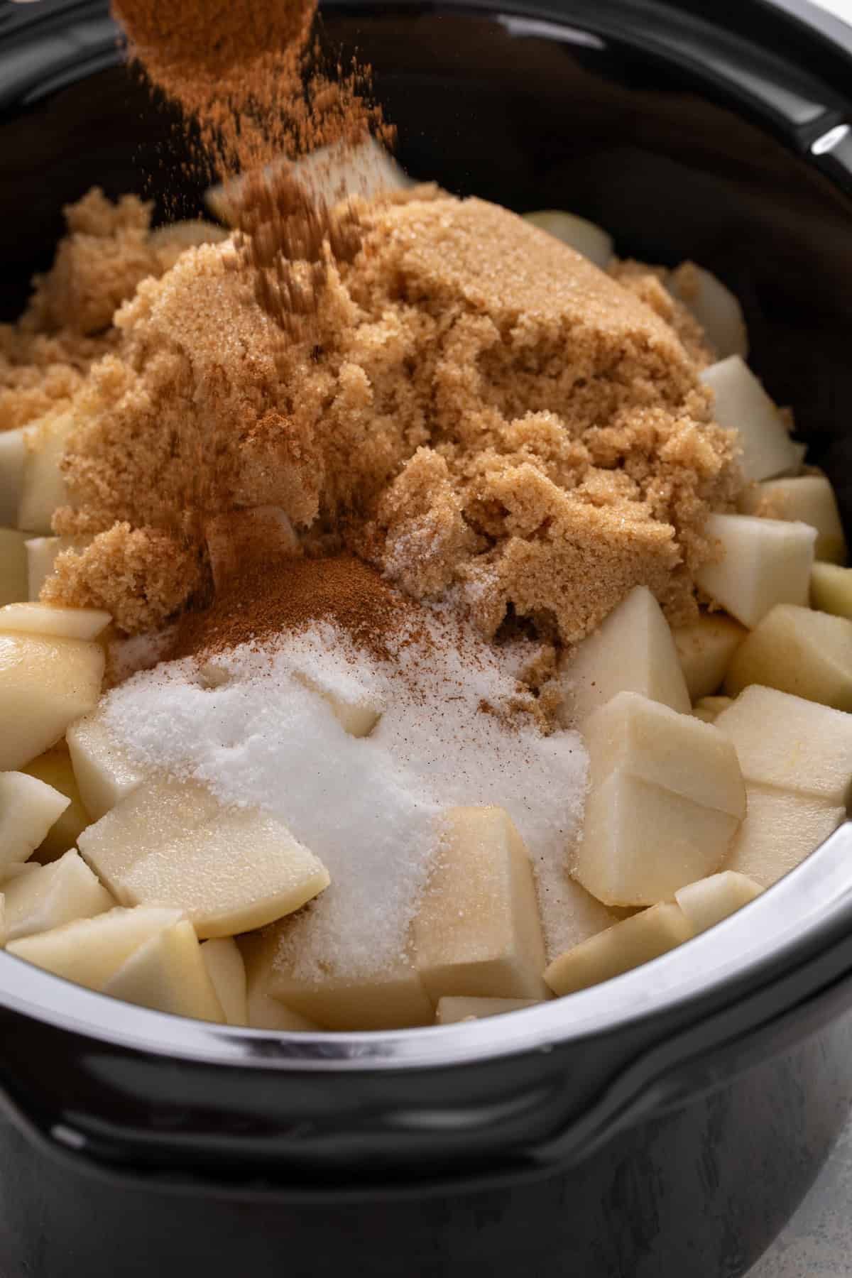 Ingredients for pear butter being added to a slow cooker.