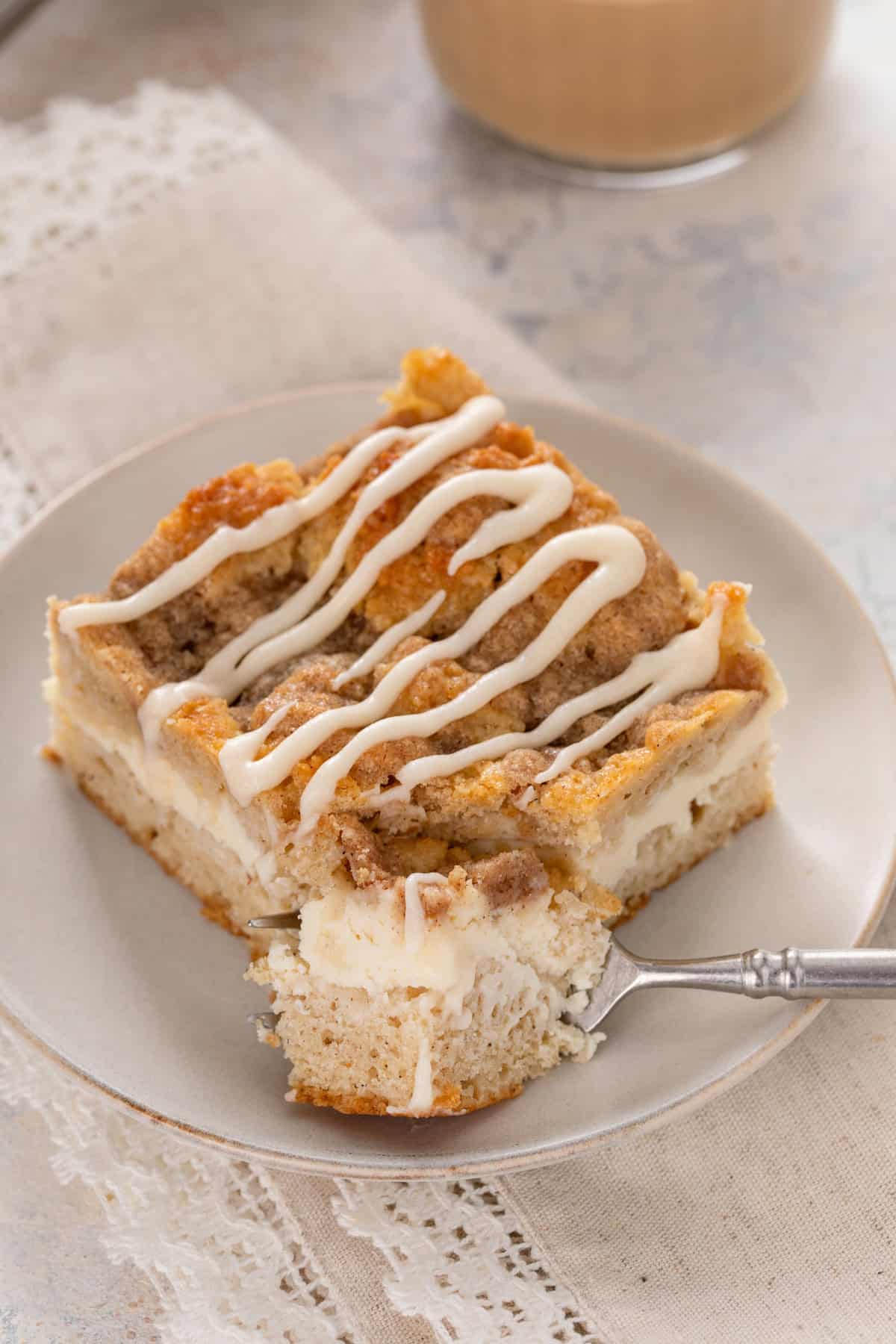 Fork cutting a bite from the corner of a slice of cream cheese coffee cake.