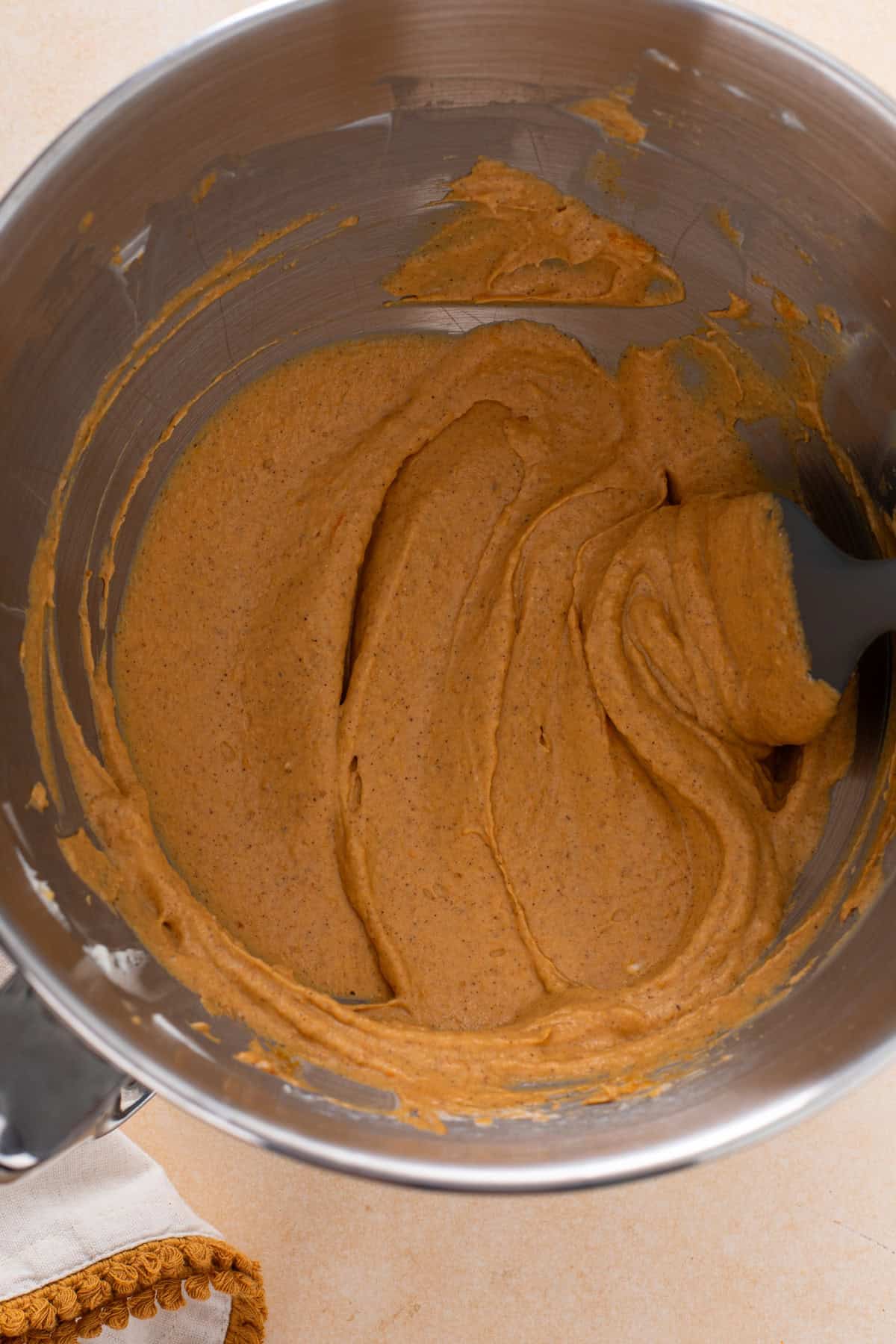 Pumpkin mixed into cream cheese in a metal bowl.