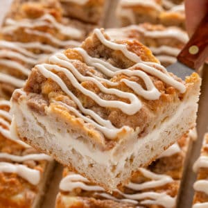 Cake server holding up a slice of cream cheese coffee cake.