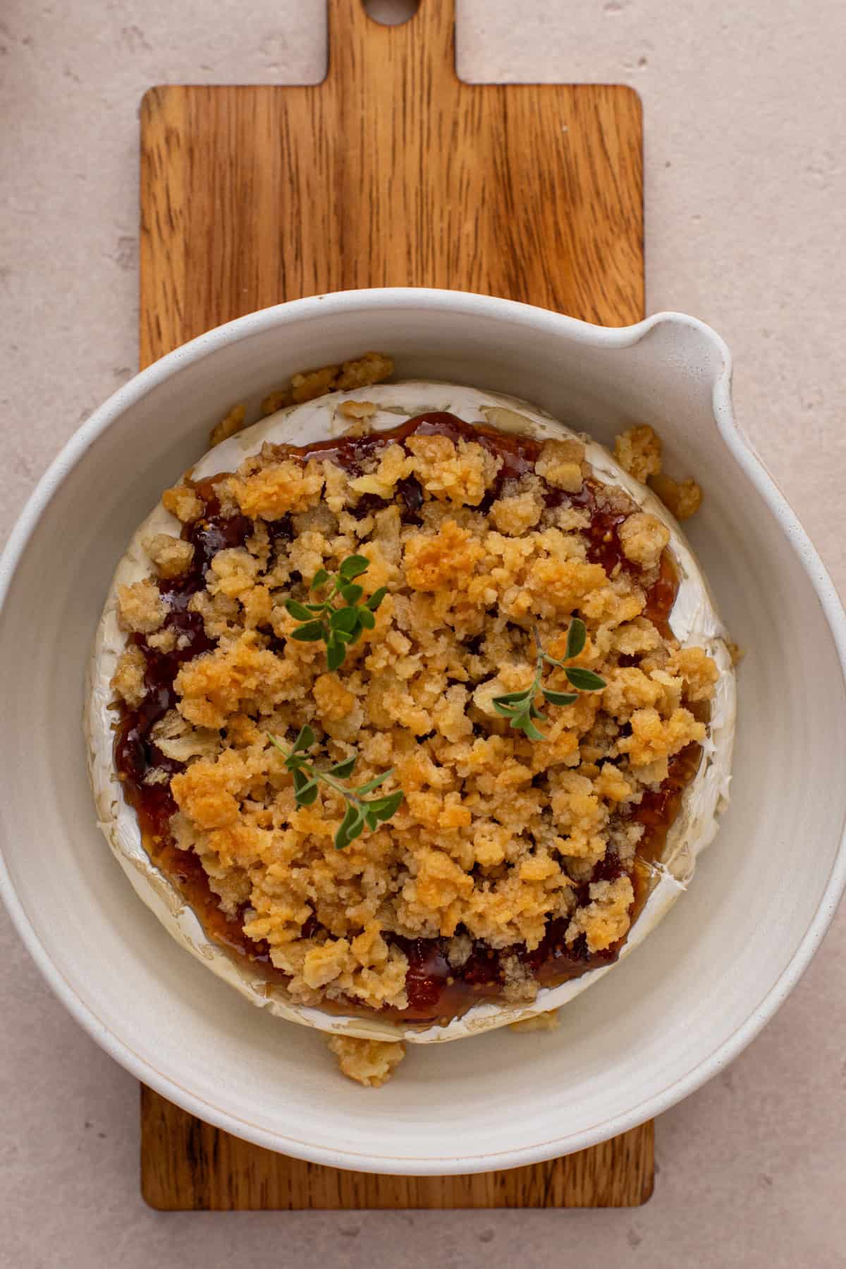 Baked brie with jam in a baking dish, cooling on a wooden board.