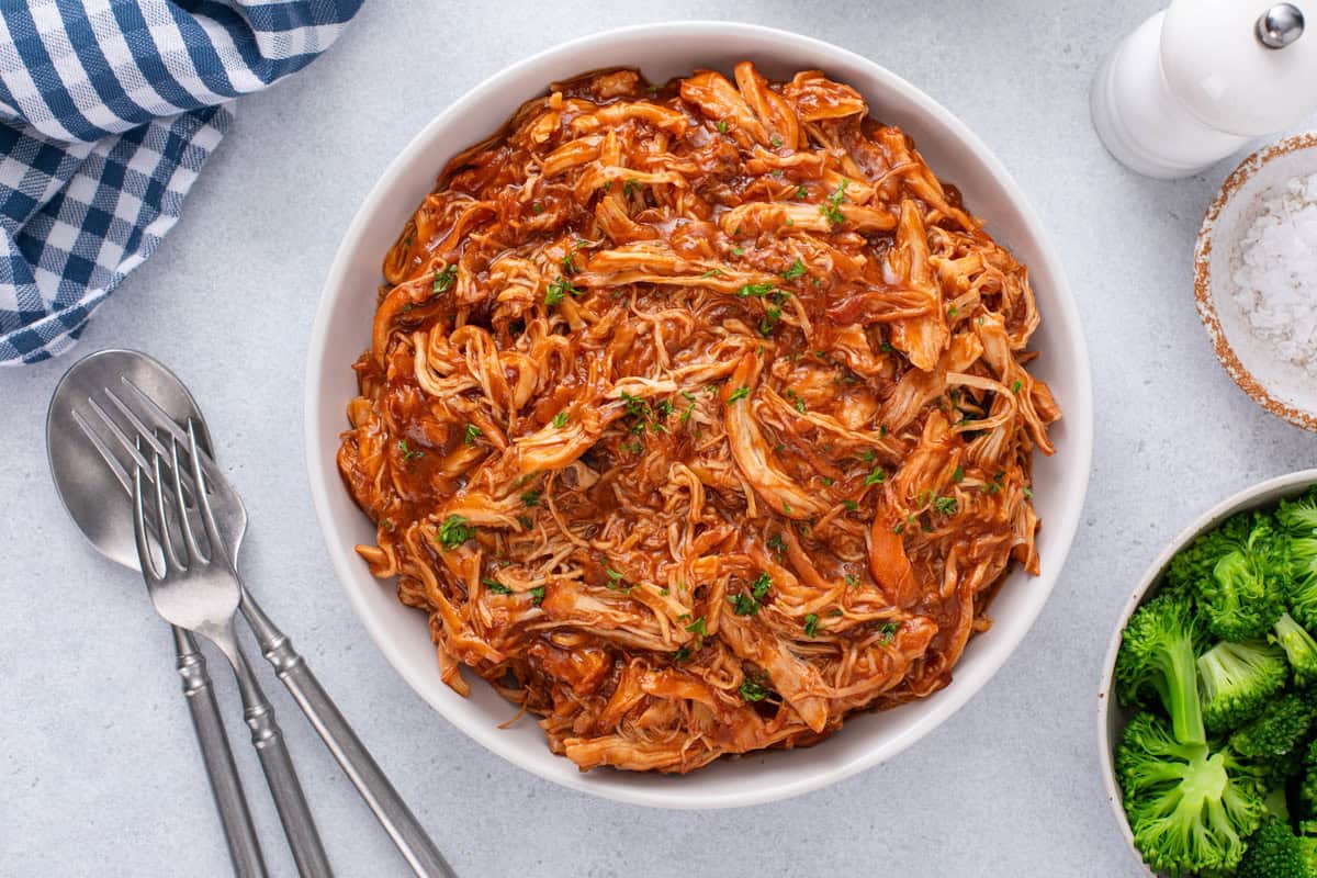 Shredded cranberry chicken with sauce in a white bowl.