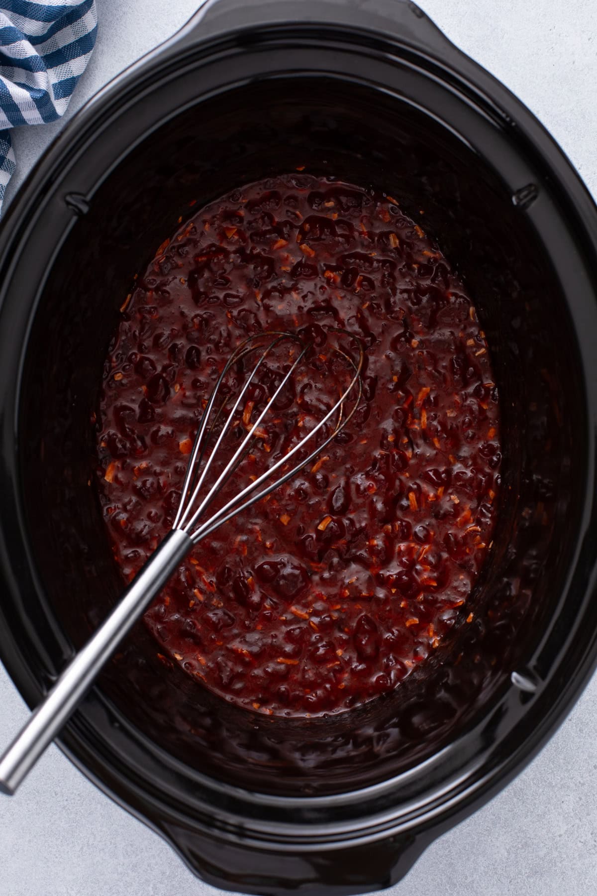 Sauce for cranberry chicken whisked in the crock of a slow cooker.
