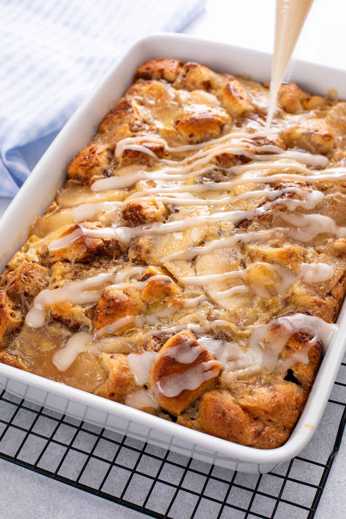 Icing being drizzled over a pan of cinnamon roll casserole.