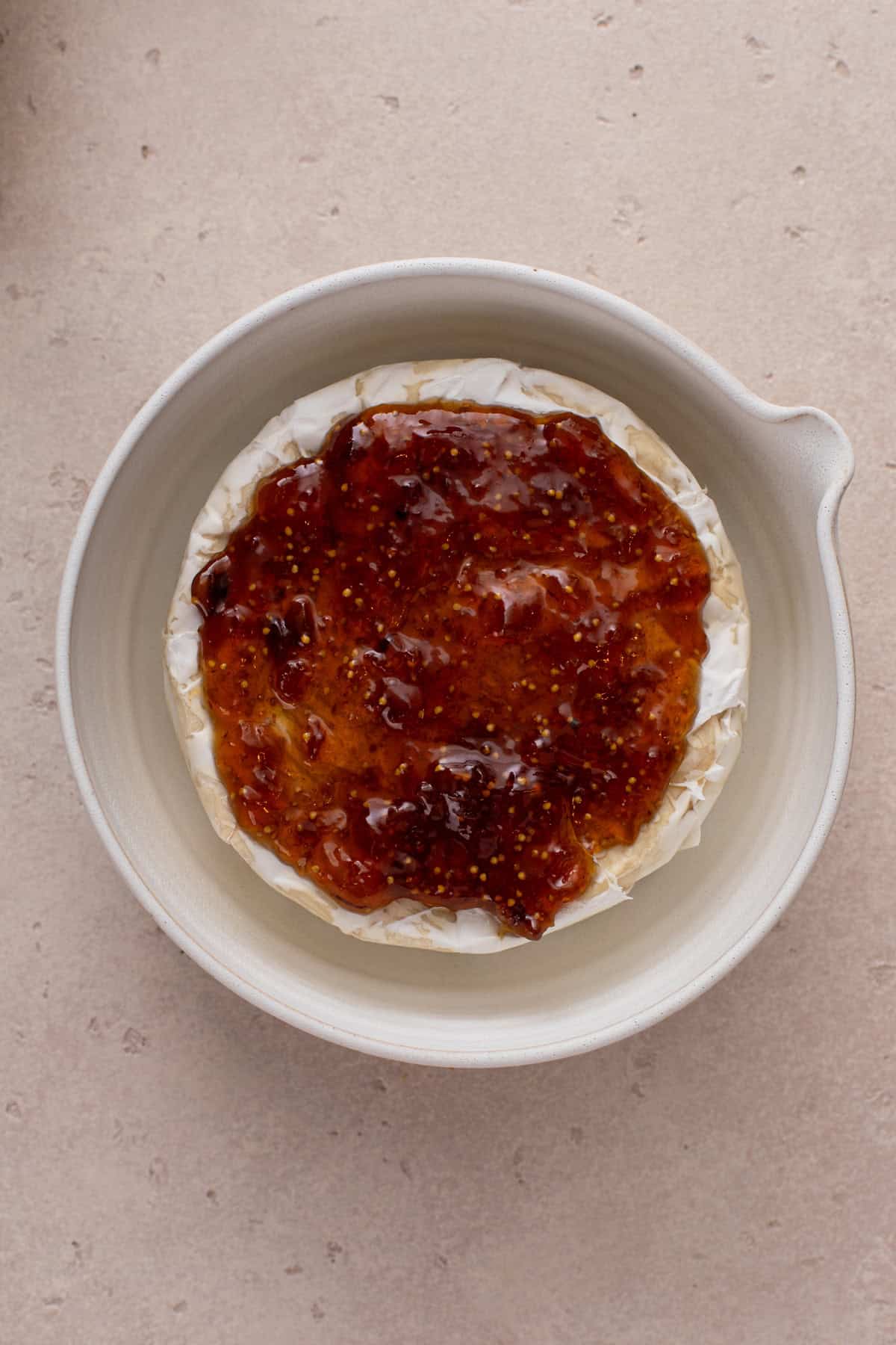 Jam spread over a wheel of brie in a baking dish.
