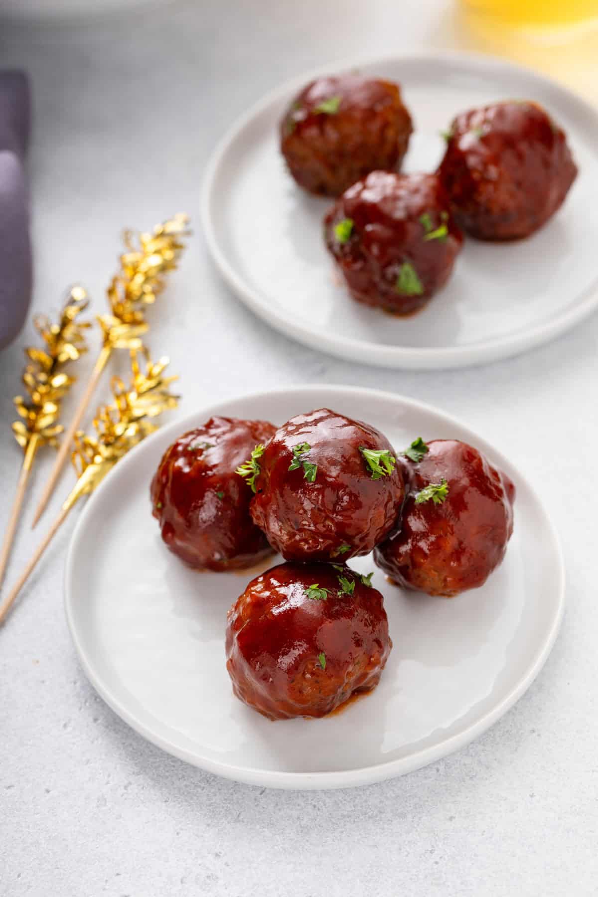 Two white plates, each holding several cranberry meatballs.