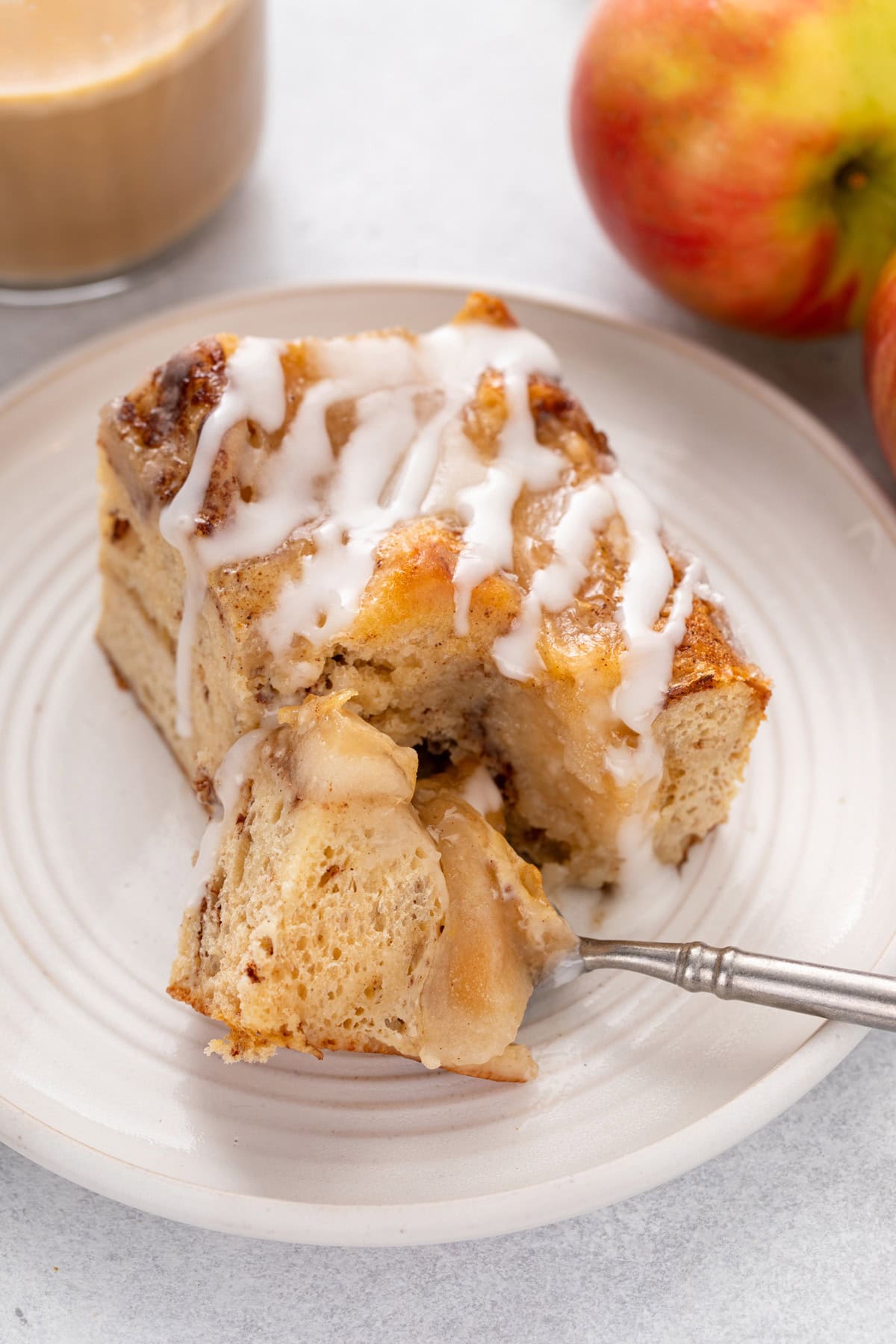 Fork cutting a bite from a piece of cinnamon roll casserole on a white plate.