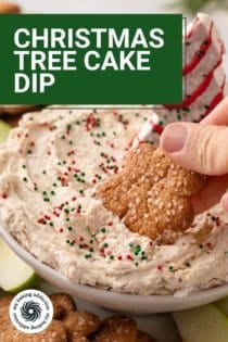 Person dipping a gingersnap cookie into a bowl of christmas tree cake dip. Text overlay includes recipe name.