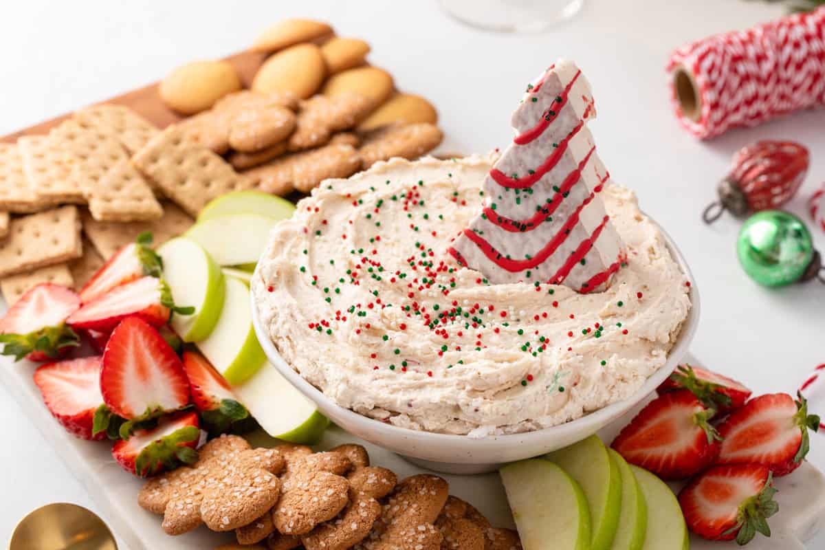 White bowl filled with little debbie christmas tree cake dip, garnished with red and green sprinkles and a whole little debbie christmas tree cake.
