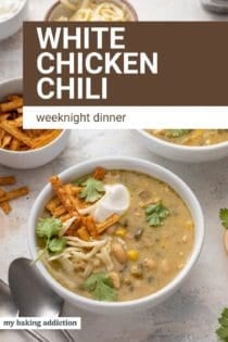 Spoon next to a bowl of white chicken chili garnished with sour cream, cilantro, and tortilla strips. Text overlay includes recipe name.
