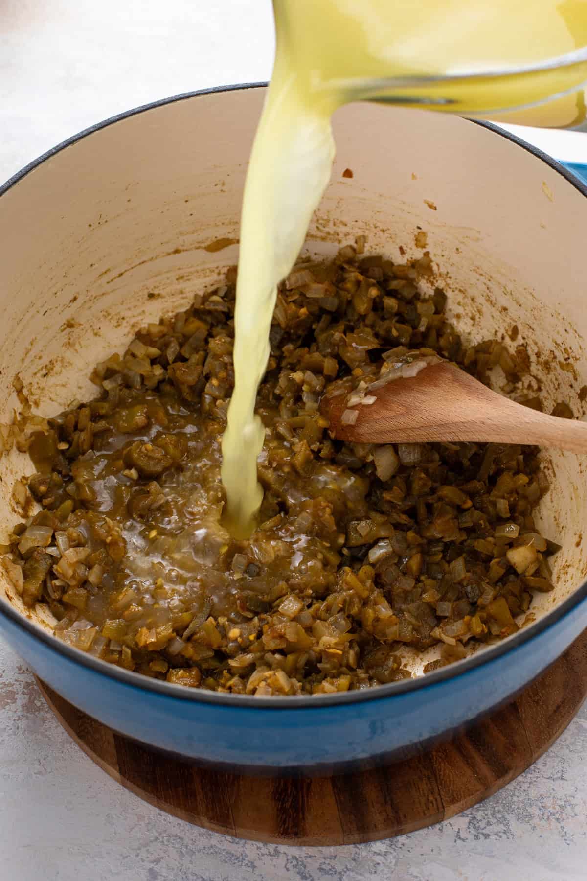 Chicken stock being added to a dutch oven of sauteed aromatics.