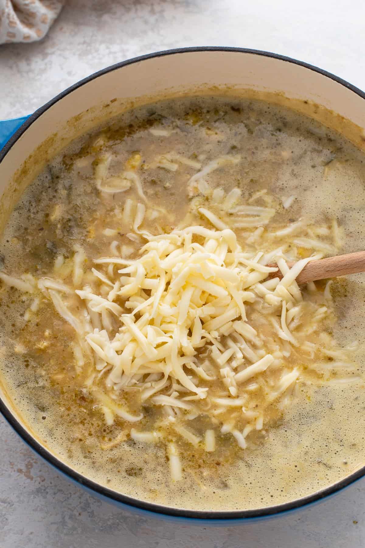 Shredded monterey jack cheese being added to a pot of chicken chili.