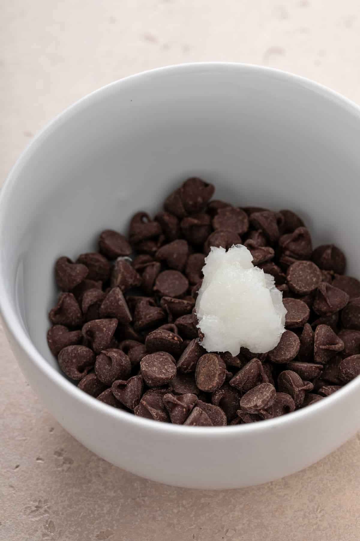 Chocolate chips and coconut oil in a white bowl.