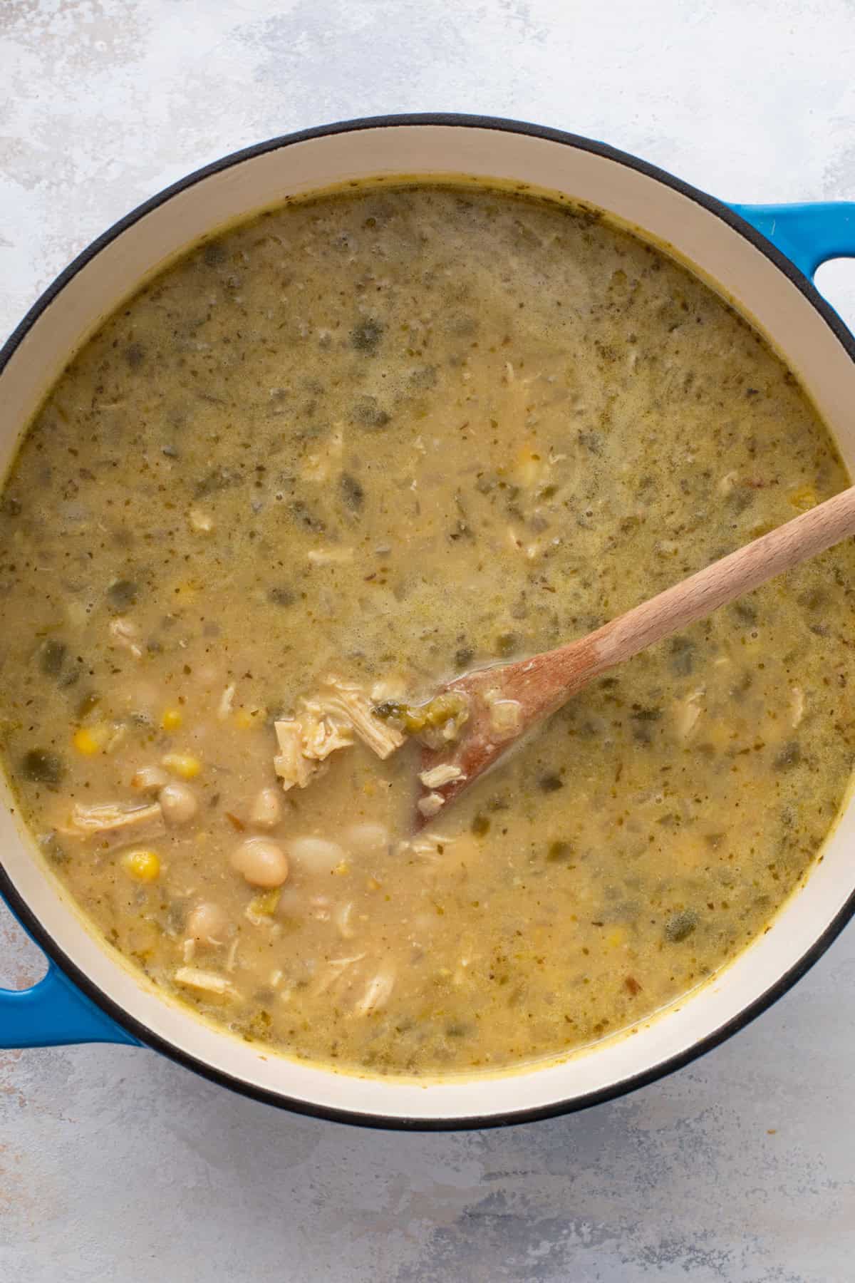 Wooden spoon stirring a pot of whit chicken chili.