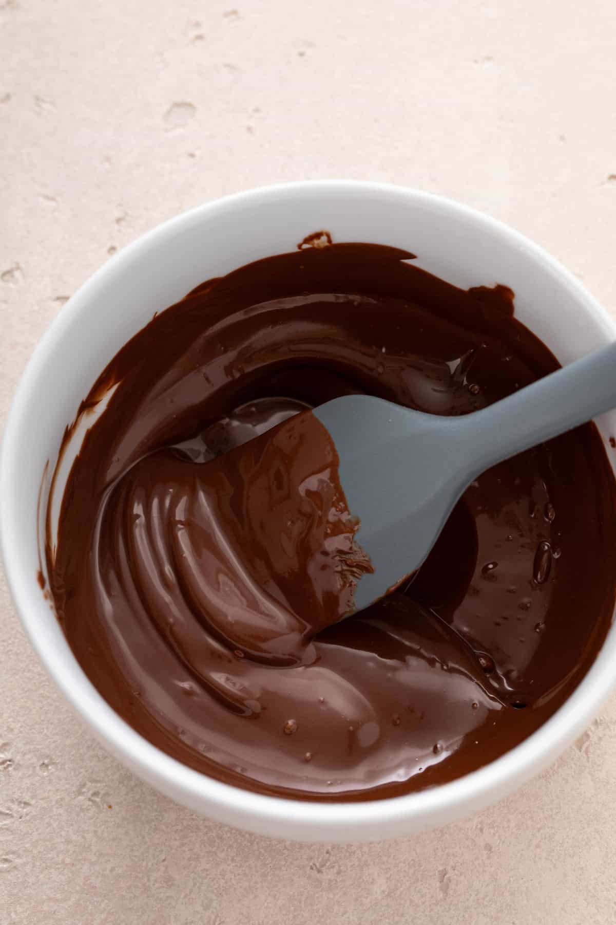 Melted chocolate being stirred with a spatula in a white bowl.