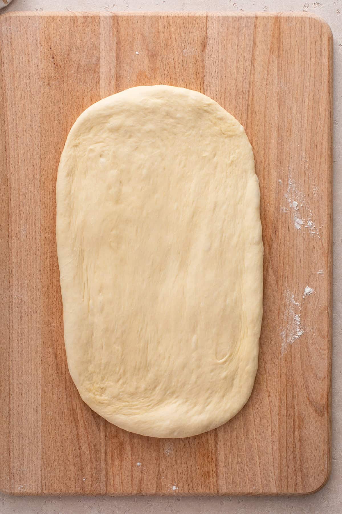 Dough for potato bread rolled into a rectangle on a wooden board.