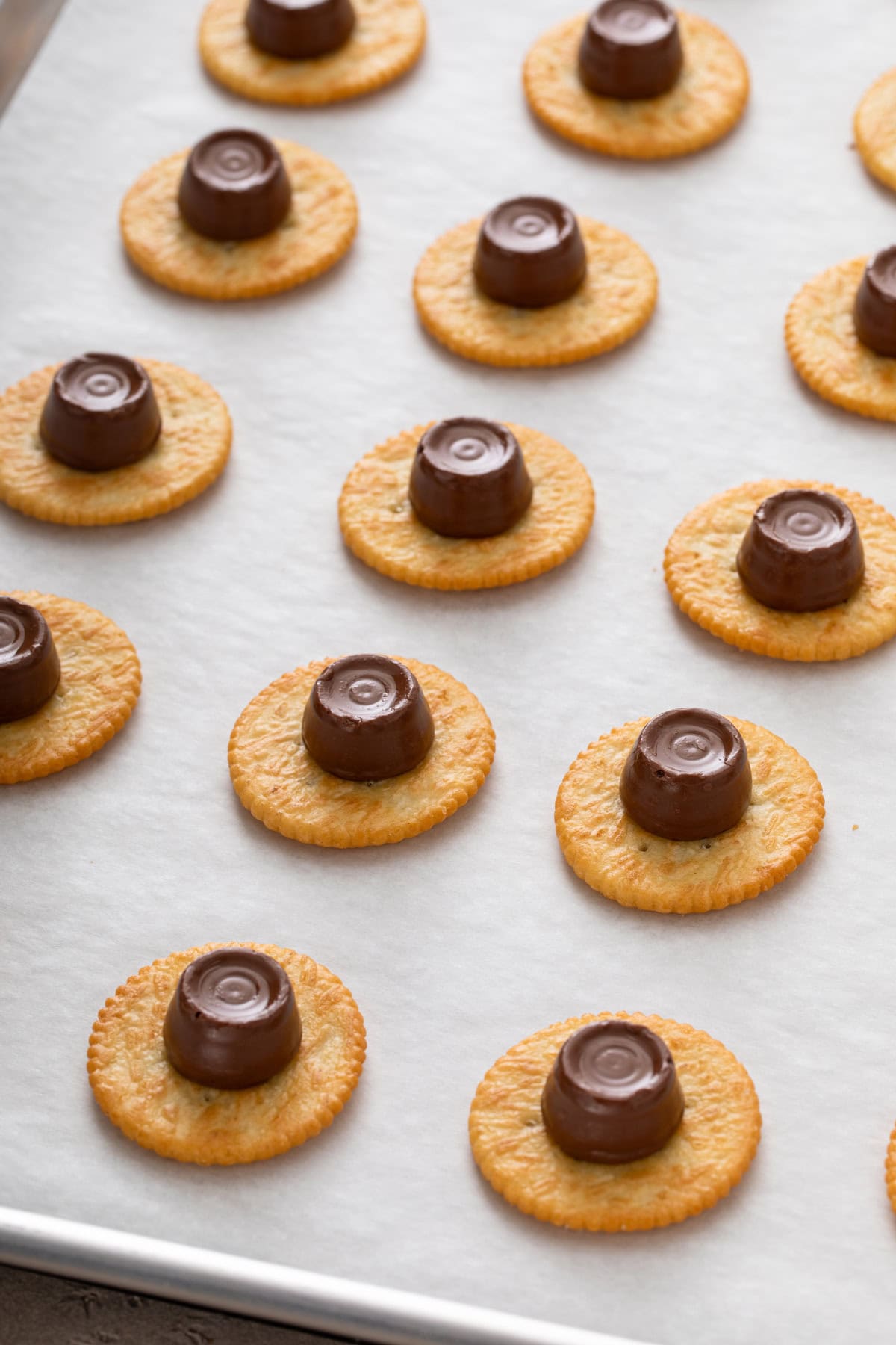 Rolo candy set in the center of ritz crackers on a parchment-lined baking sheet.