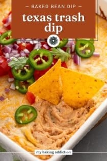 Two tortilla chips in a pan of Texas trash bean dip, garnished with sliced jalapeños, tomatoes, and red onions. Text overlay includes recipe name.
