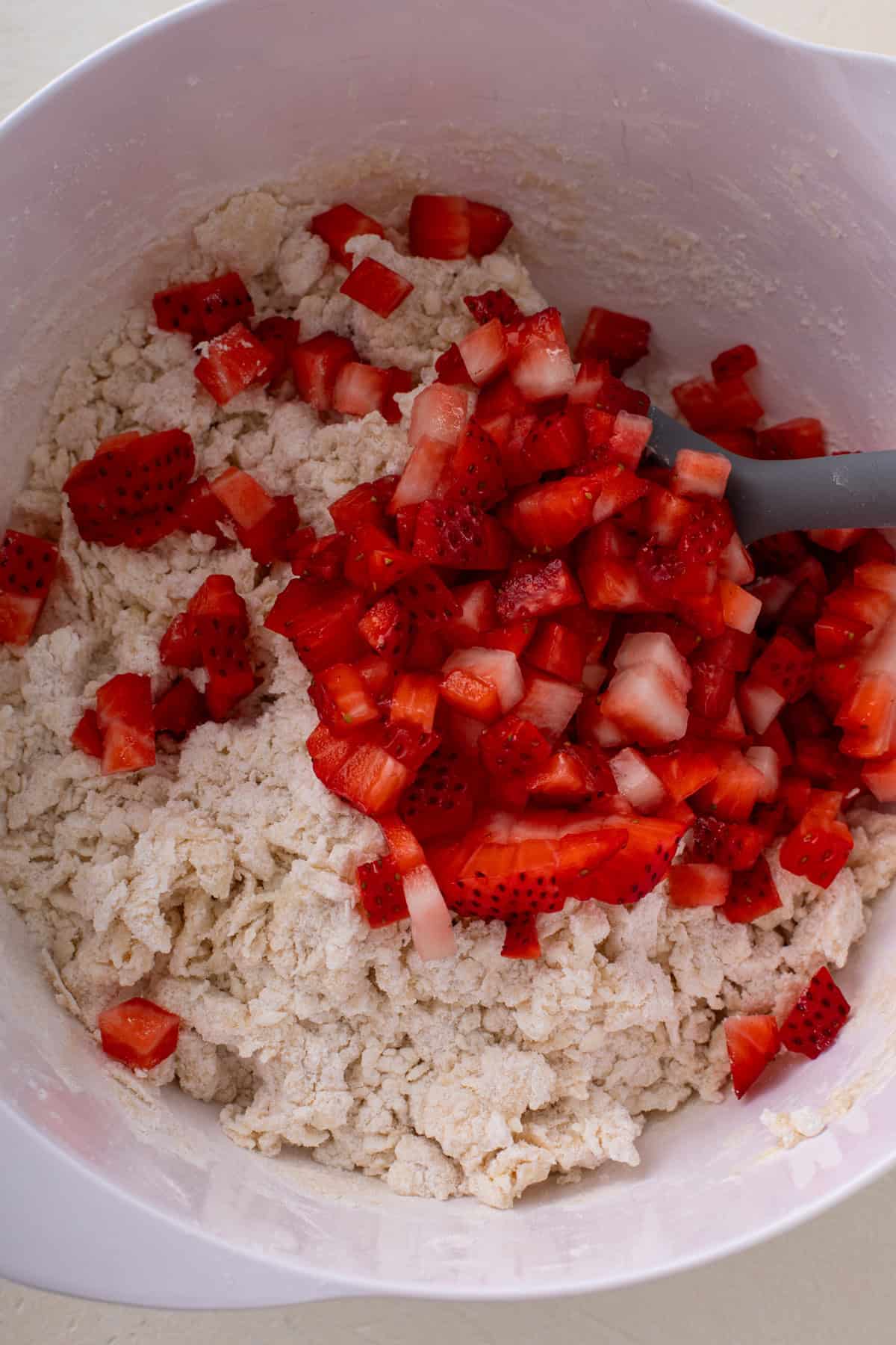 Diced strawberries added to mixed scone dough in a white bowl.