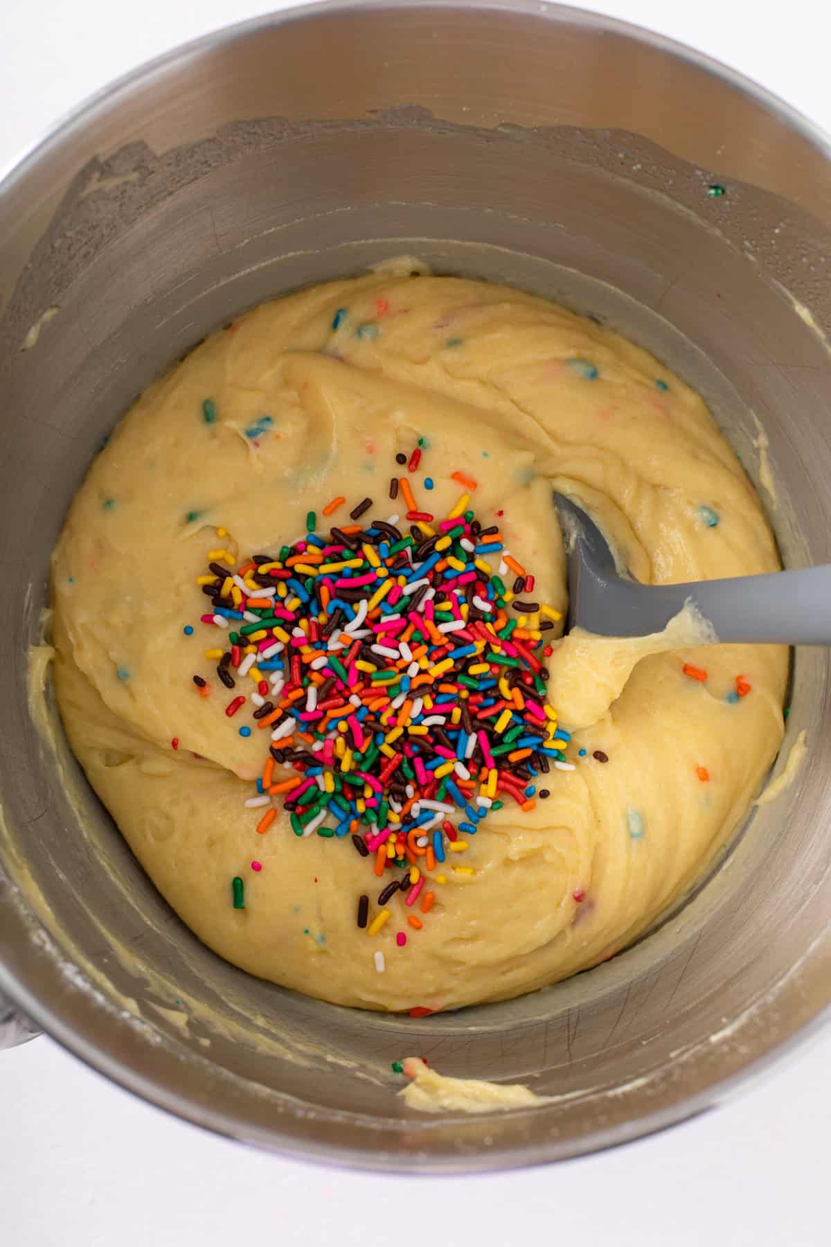 Rainbow sprinkles being added to funfetti cake batter in a steel mixing bowl.