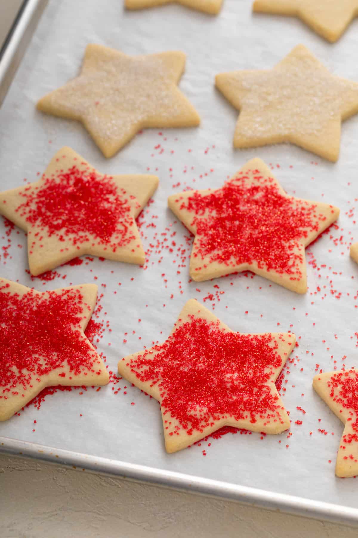 Baked star cutout cookies on a parchment lined baking sheet, decorated with red and white sparkling sugar.