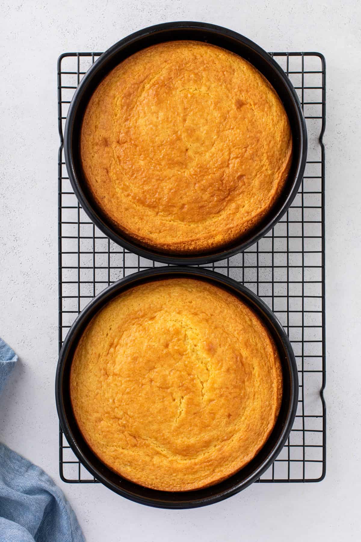 Two yellow cake layers cooling in the pans on a wire rack.