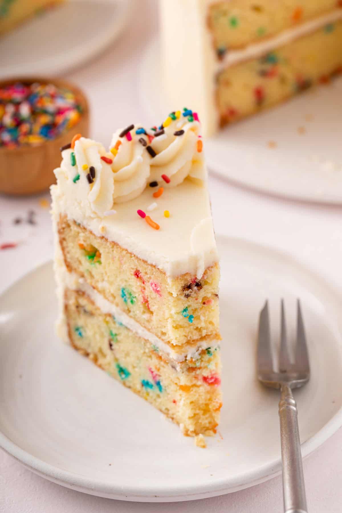 Plated slice of funfetti layer cake with a bite taken from the slice.