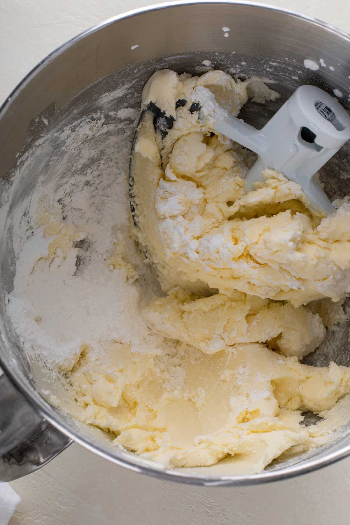 Paddle attachment for a stand mixer in a bowl with butter and powdered sugar that has been mixed together.