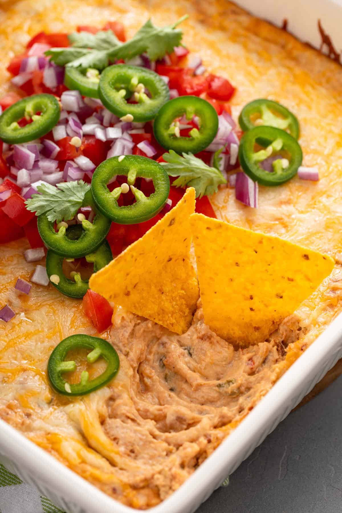 Two tortilla chips in a pan of Texas trash bean dip, garnished with sliced jalapeños, tomatoes, and red onions.