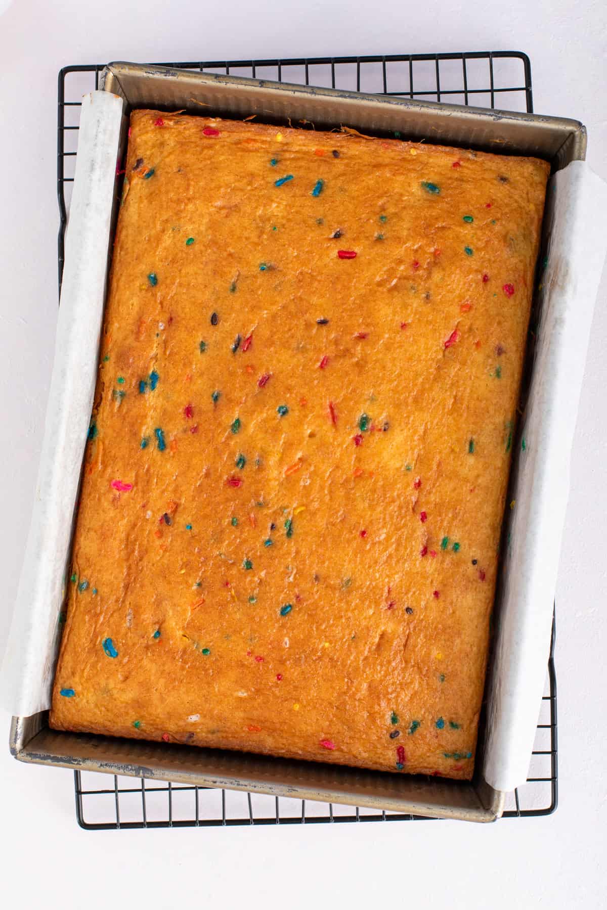 Baked funfetti sheet cake cooling in the pan on a wire rack.