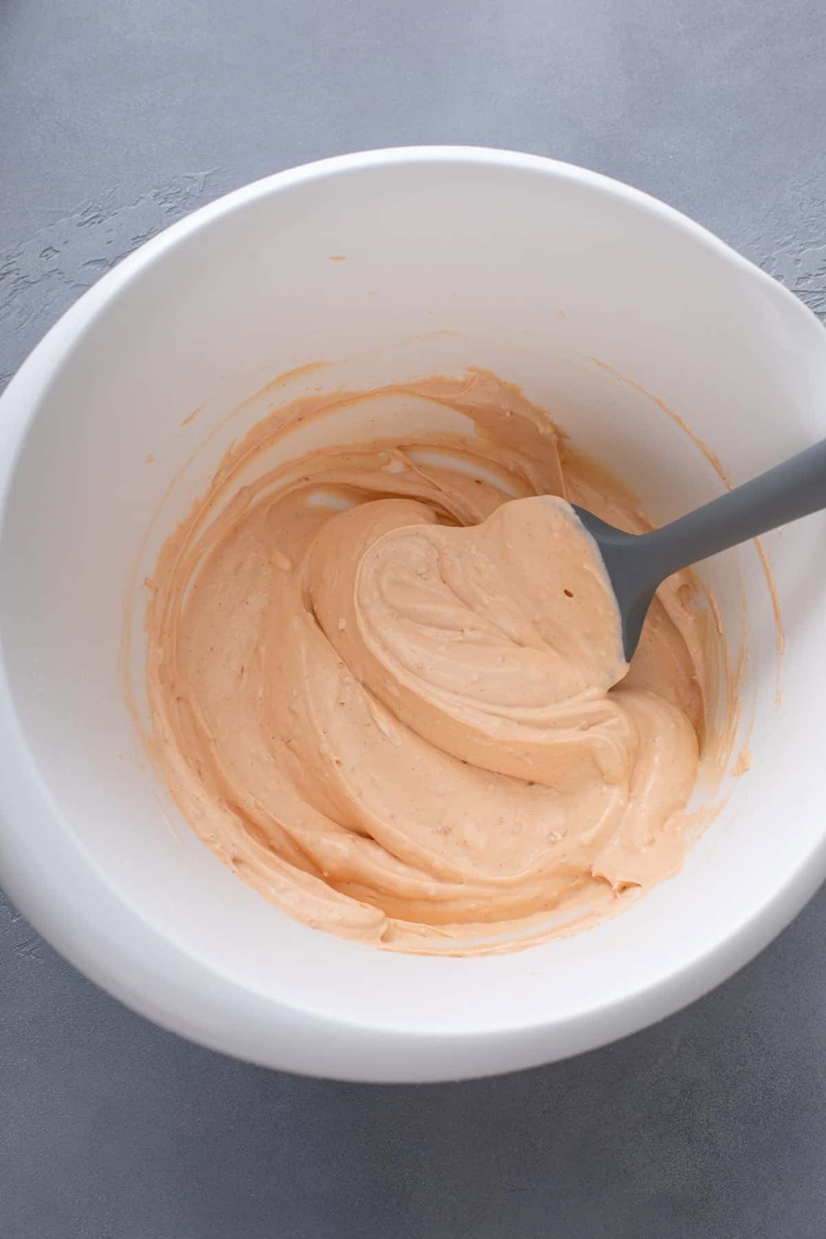 Spatula mixing cream cheese, sour cream, and taco seasoning in a white bowl.