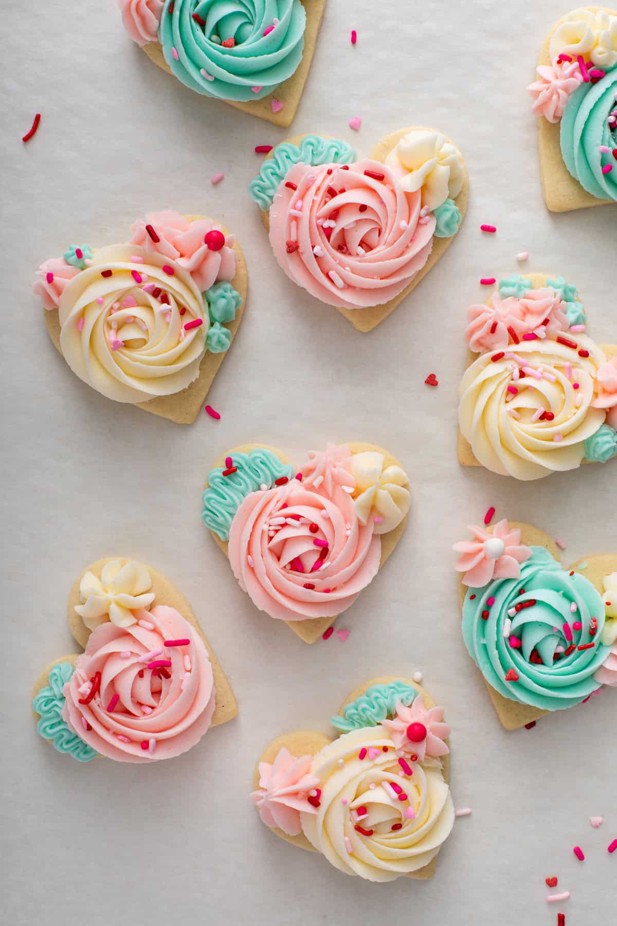 Heart-shaped sugar cookies topped with pink, white, and mint green sugar cookie frosting and sprinkles.