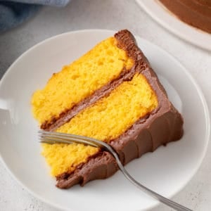 Fork cutting a bite from a slice of yellow cake on a white plate.
