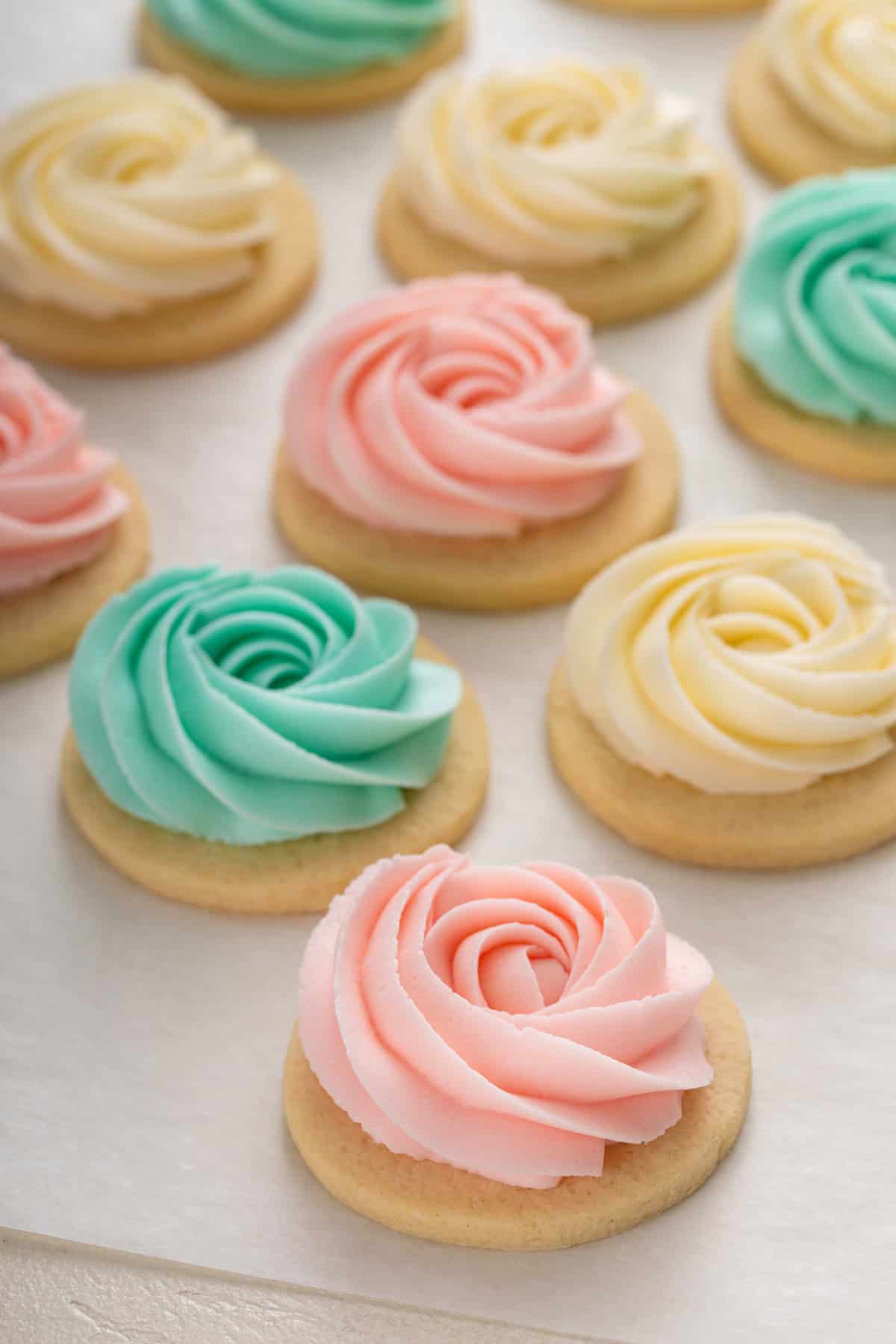 Sugar cookie frosting piped into rosettes in three different colors on round sugar cookies.