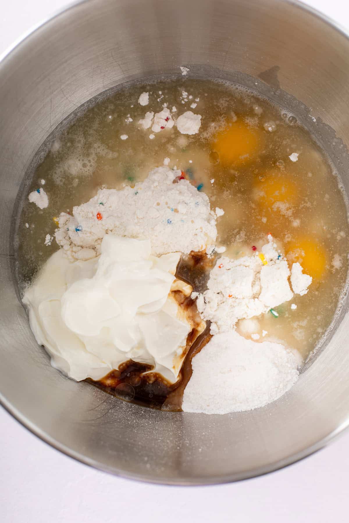 Ingredients for easy funfetti cake batter added to the bowl of a stand mixer.